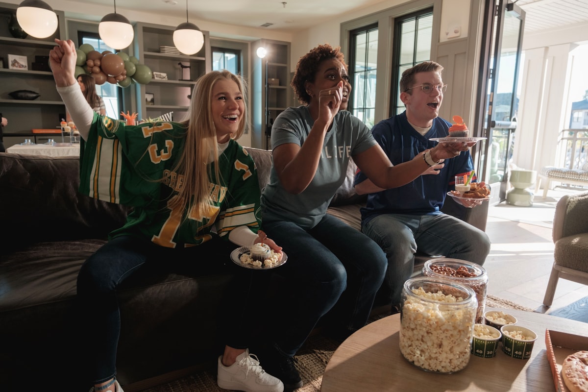 Friends in football jerseys cheering with snacks at a draft party