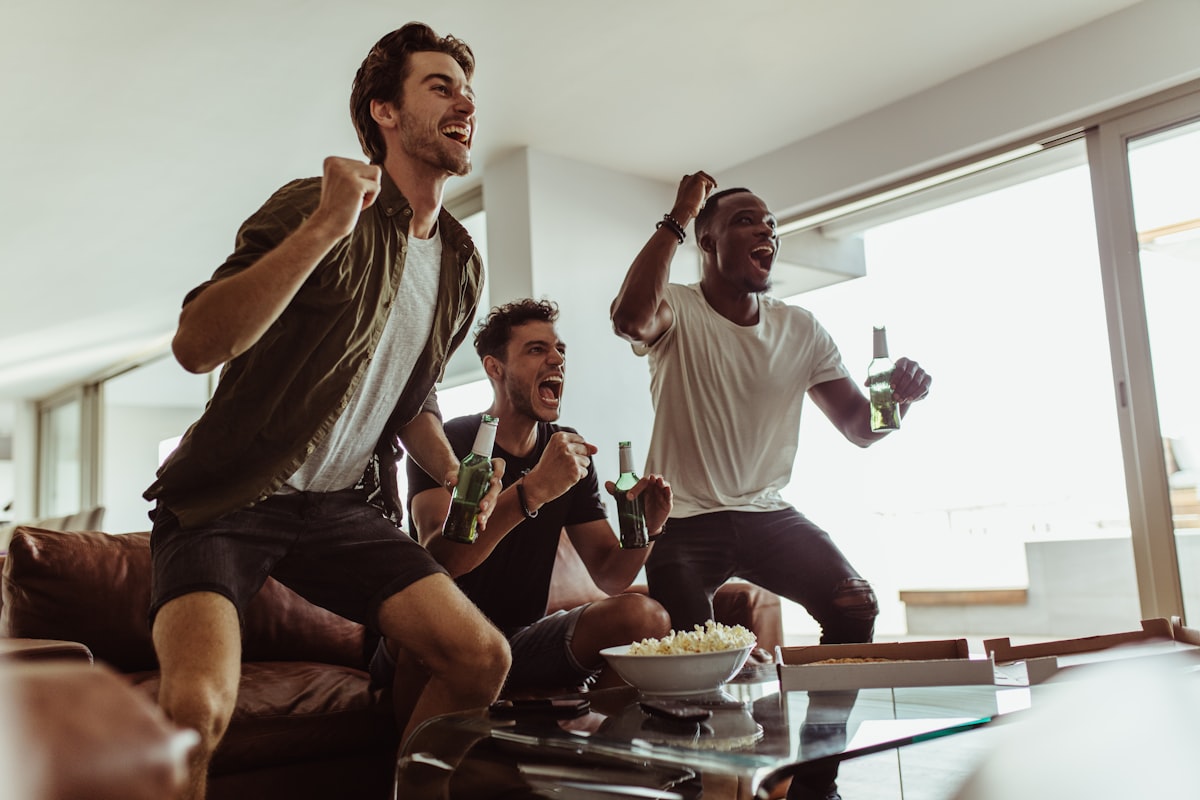 Three friends jumping up and cheering while watching a game at home