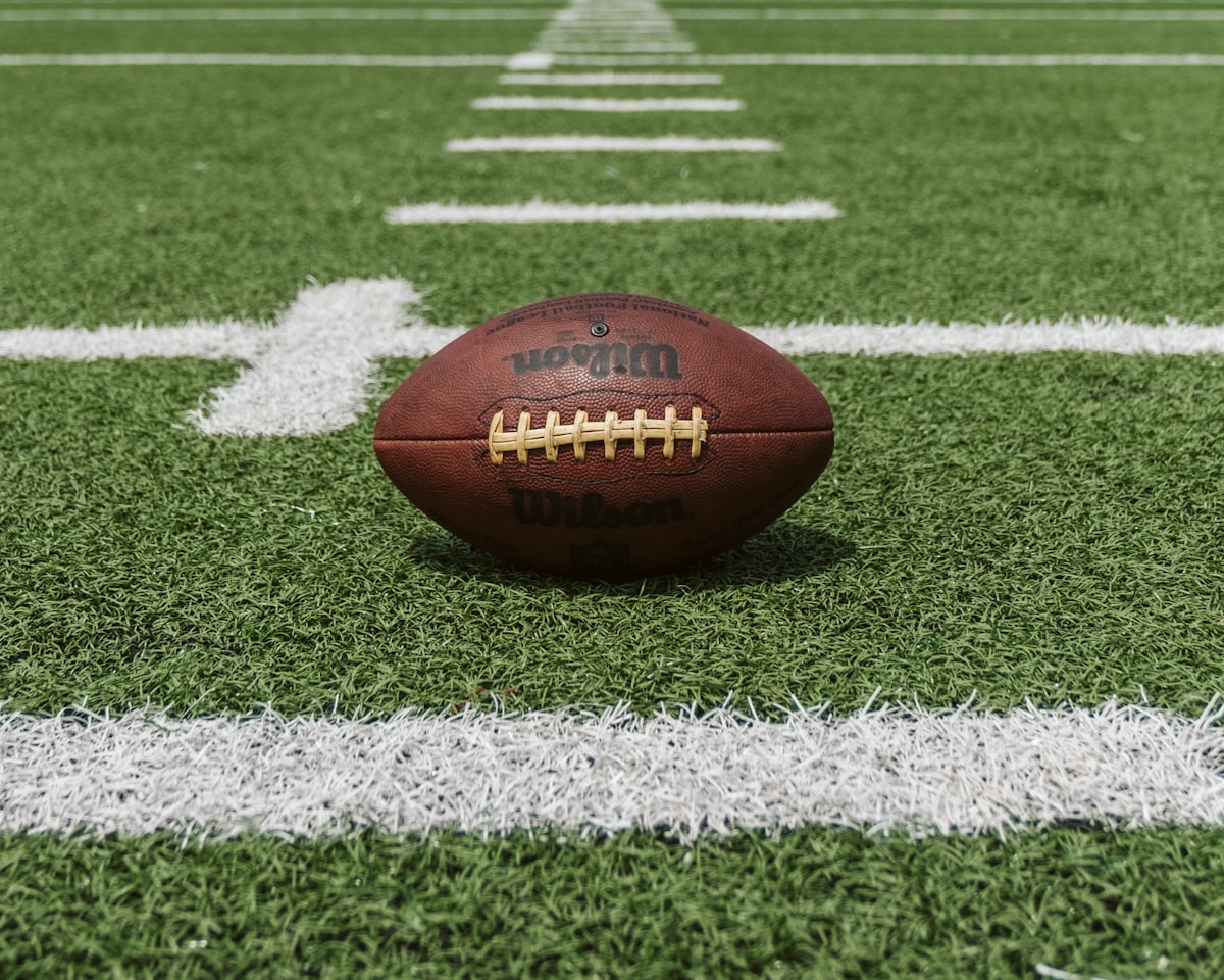 An American football on a green field with yard lines